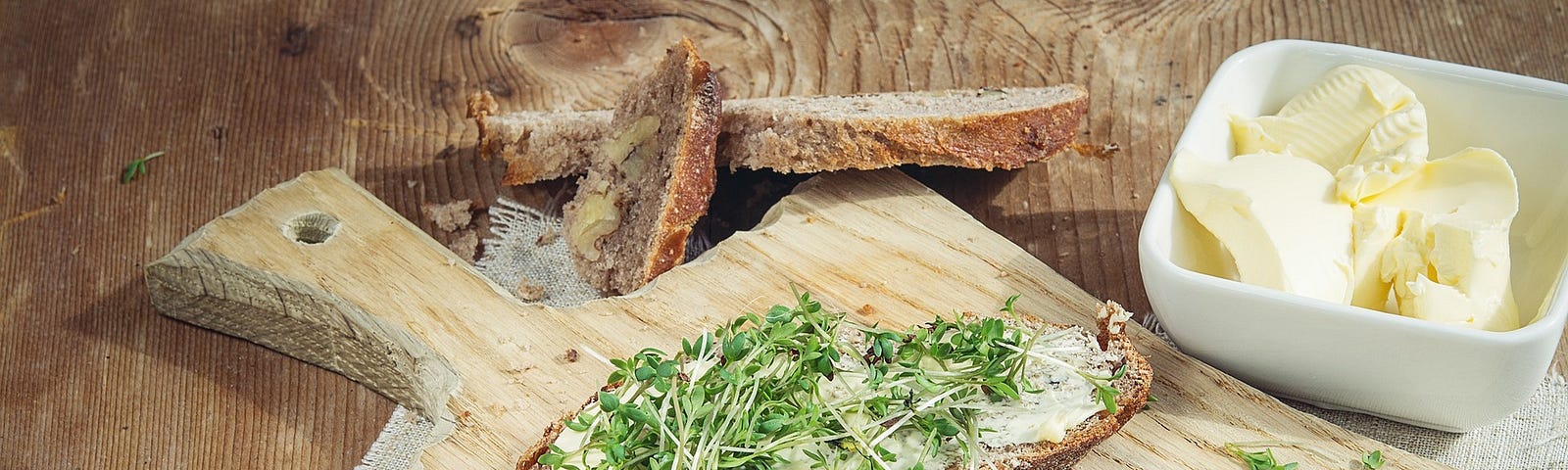 Picture of a kitchen cutting board with two slices of buttered bread generously covered with watercress.