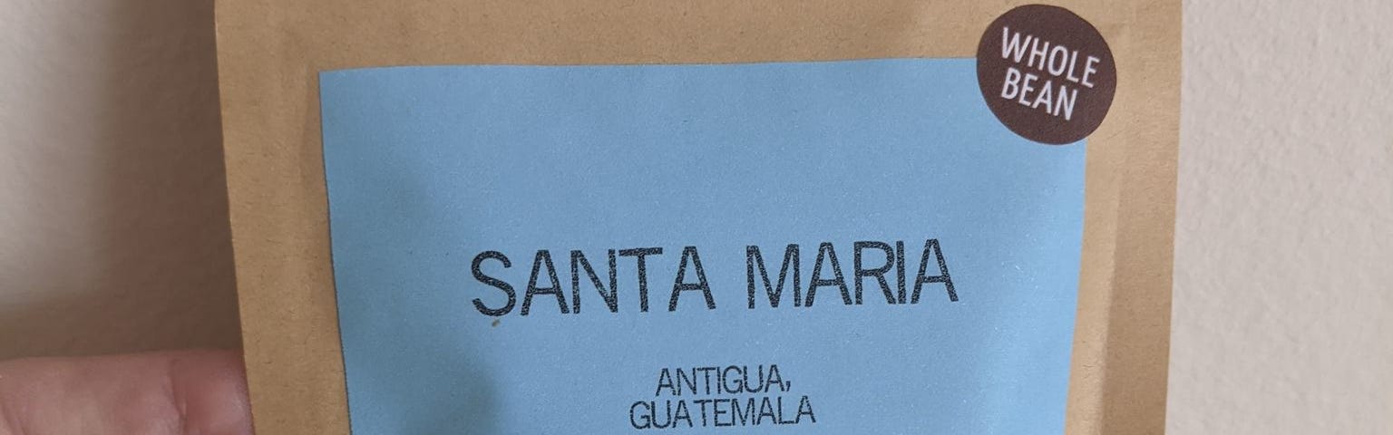 Bag of coffee beans. Labels state “Whole Bean”, “Santa Maria” “Antigua Guatemala” includes tasting notes and roast date of the coffee.