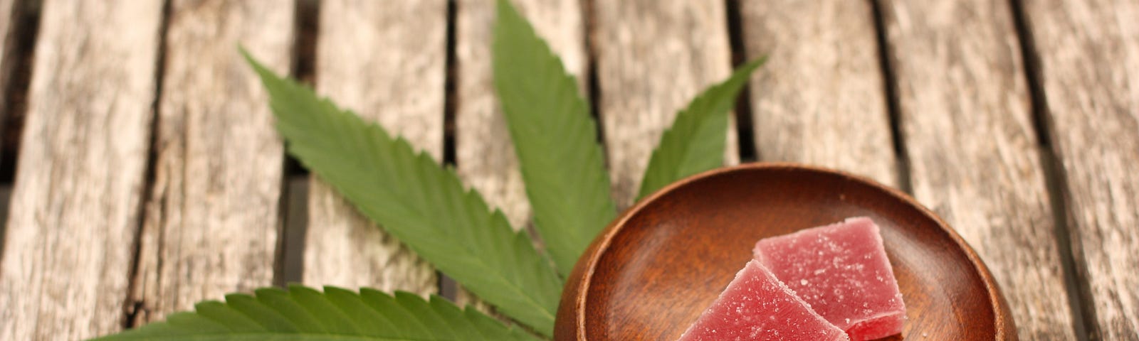 Marijuana leaf and a dish of cannabis edibles on a wooden table. Dispensary warning