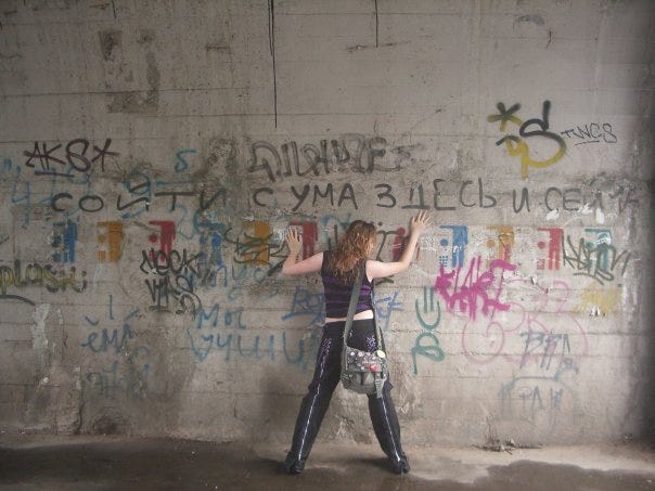 A photo with Insane Linn from the back standing under a graffiti with “To get insane here and now” in Russian.