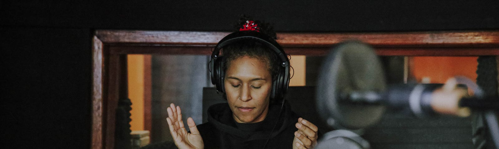 Kat in the music studio with head phones on, listening as she holds her hands up about to clap