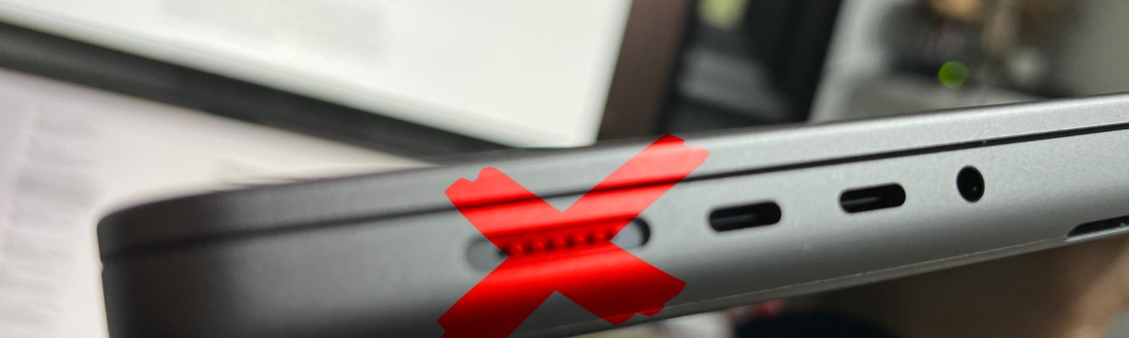 A MacBook Pro with a red painted X overlaid on the MagSafe port.