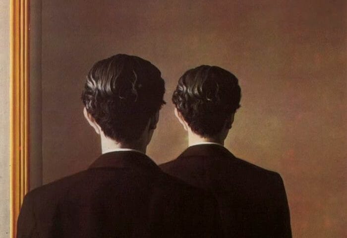 A man with his back to us, standing in front of the mirror. But, his reflection is the same — not facing us, as it should be.