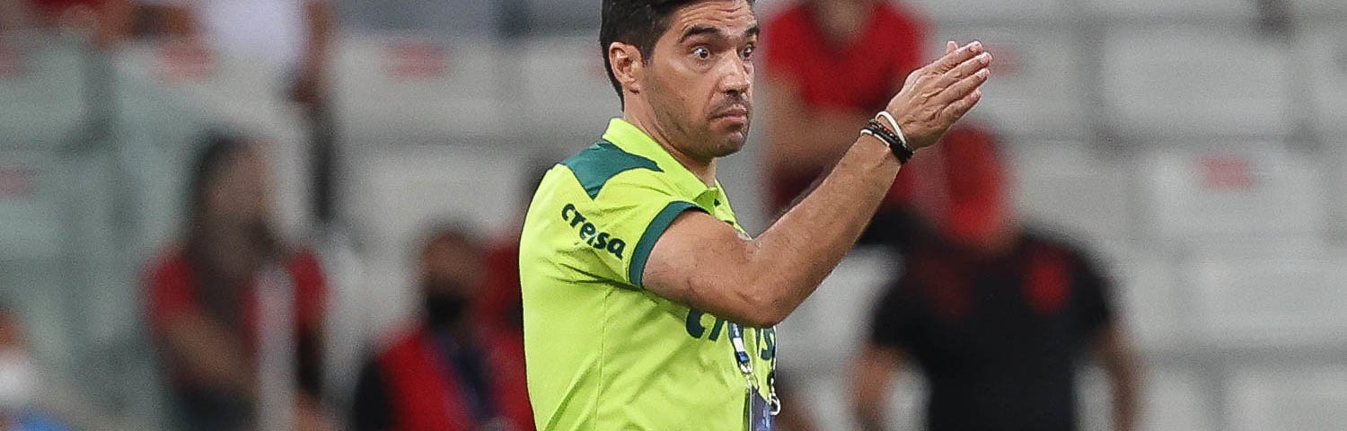 Abel Ferreira, técnico do Palmeiras, durante jogo contra o Athletico Paranaense pela Recopa Sul-Americana. Ele veste camisa verde limão e calça verde, mas aparece na imagem só da cintura para cima, com a mão direita levantada.