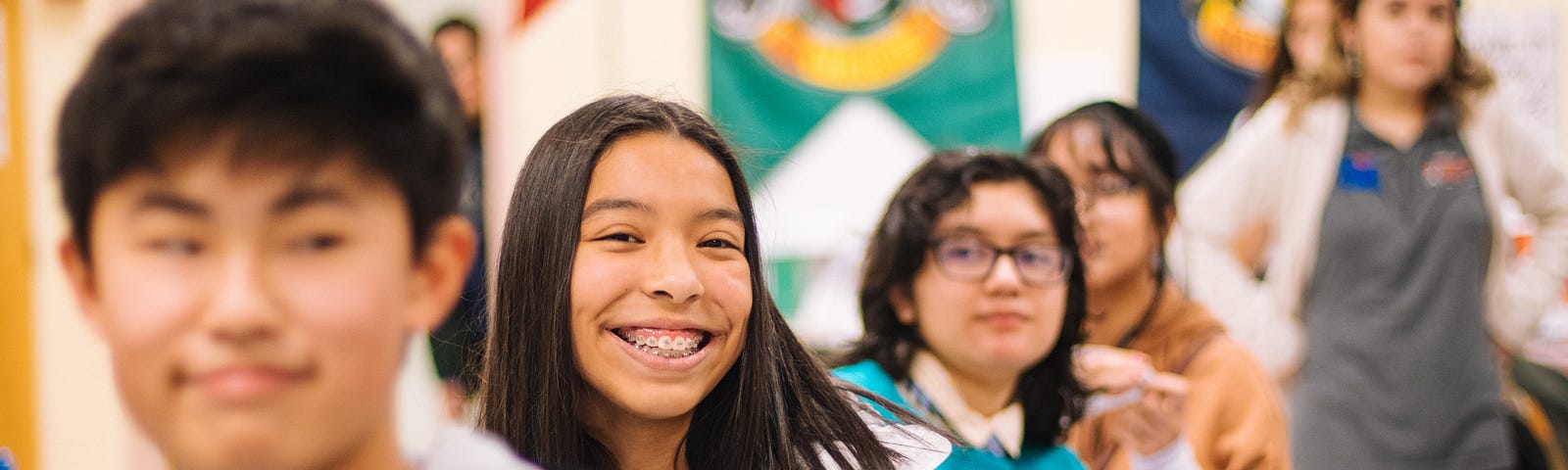 Students are seated in row in a classroom. One is smiling, the rest look bemused.