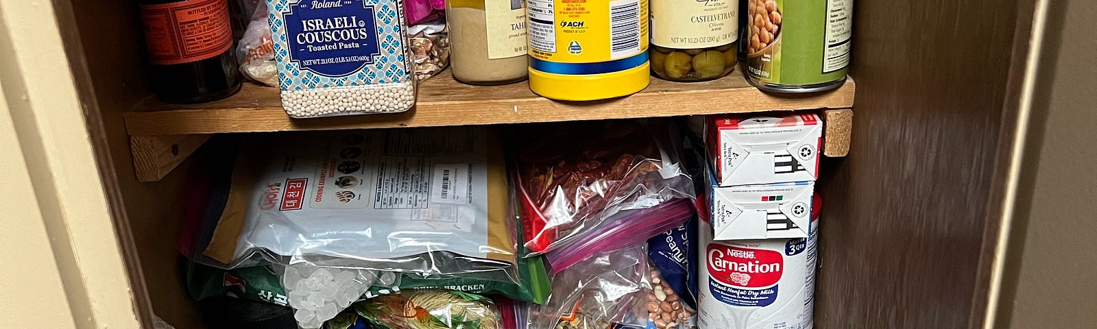 The Author’s terribly disorganized pantry cabinet containing a kitchenaid mixer and a hodgepodge of random shelf-stable ingredients.