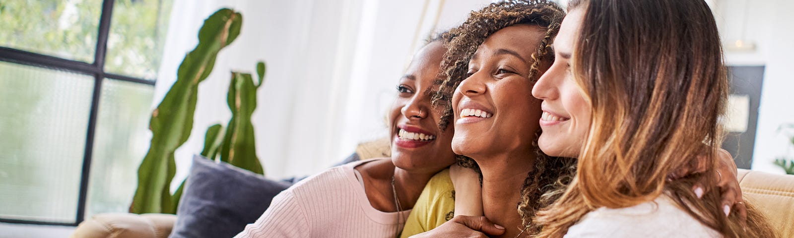 Three friends embrace and smile on a sofa.