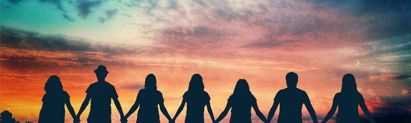 People holding hands in silhouette against sunset sky