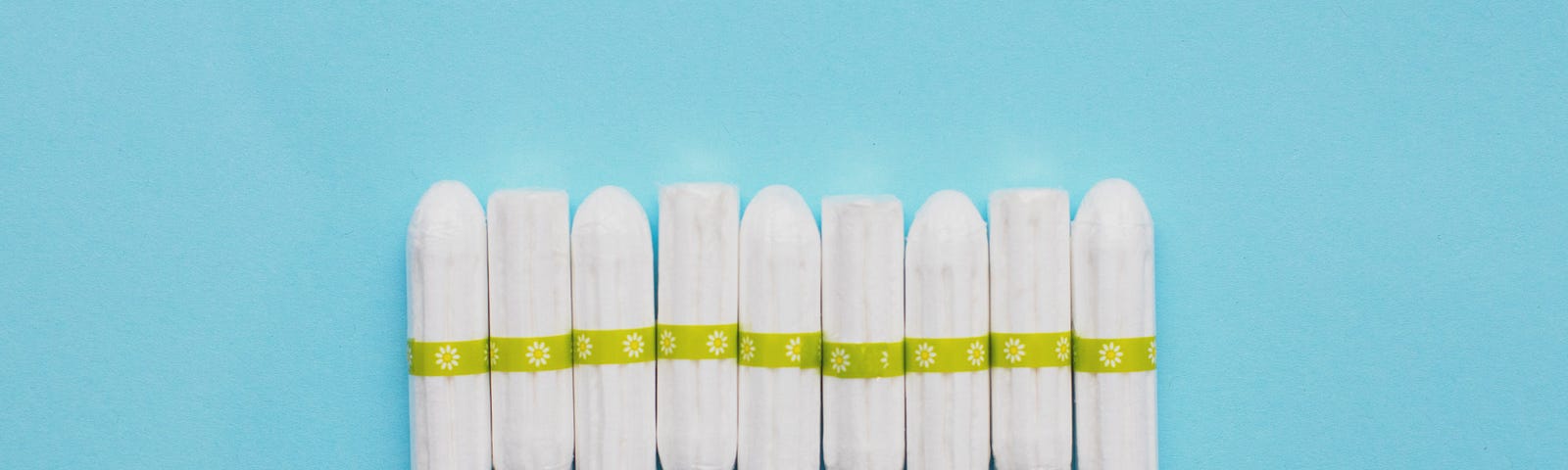 Nine tampons are lined up next to each other horizontally on a plain blue background.