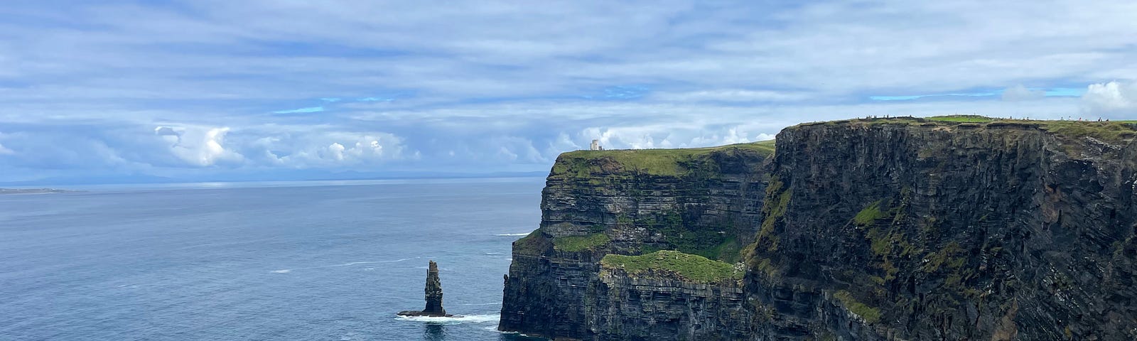 Cliffs of Moher. A rocky cliff with grass. Blue water at the bottom and blue skies overhead.