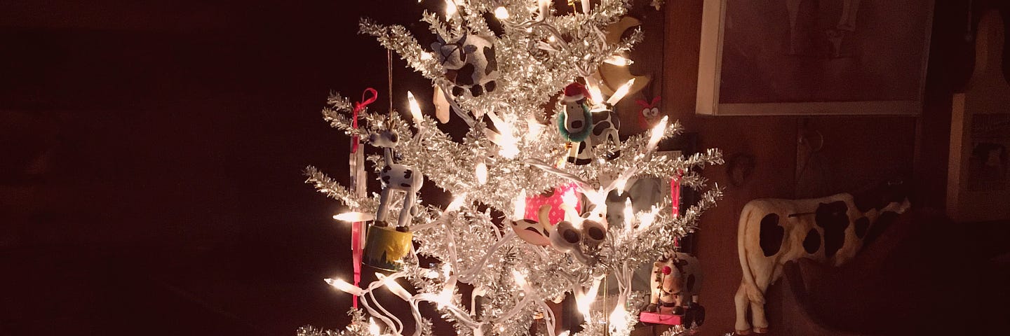 A silver-white artificial Christmas tree on a little table. The tree is covered in cow ornaments, and there are cow tchotchkes on the table and walls.