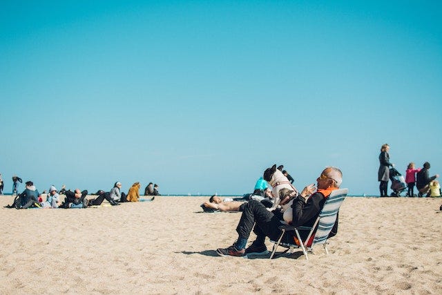 A man sitting on the beach with a dog on his lap.
