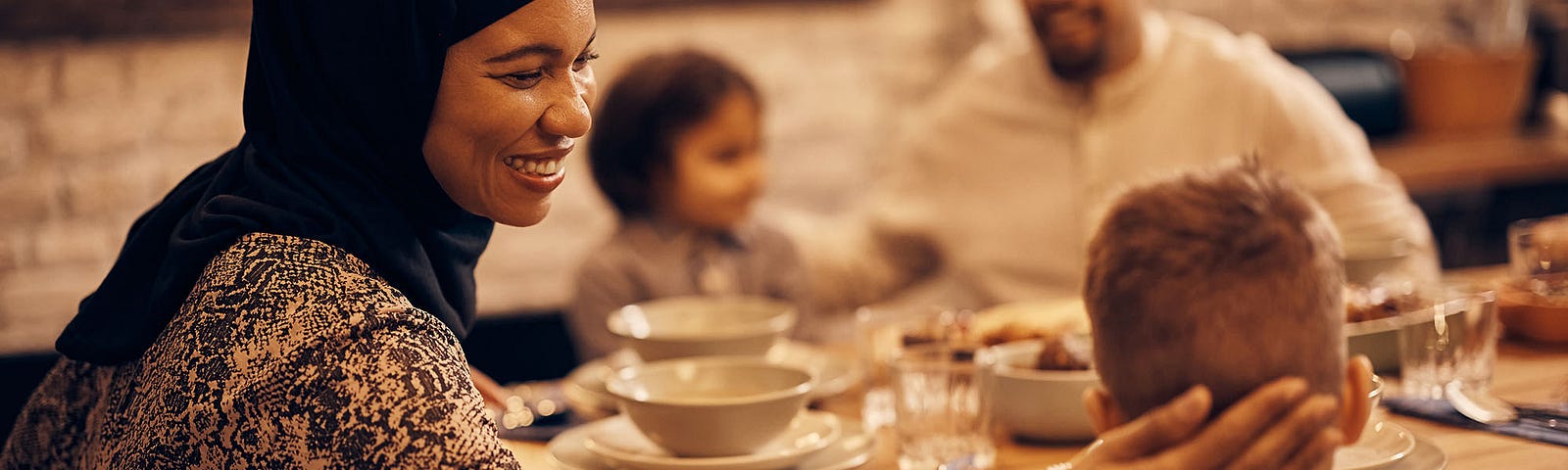 A woman is smiling at the table with her children and partner during evening mealtime.