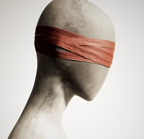 A mannequin type figure, side-view, with peach-colored blindfold over eyes and ears.