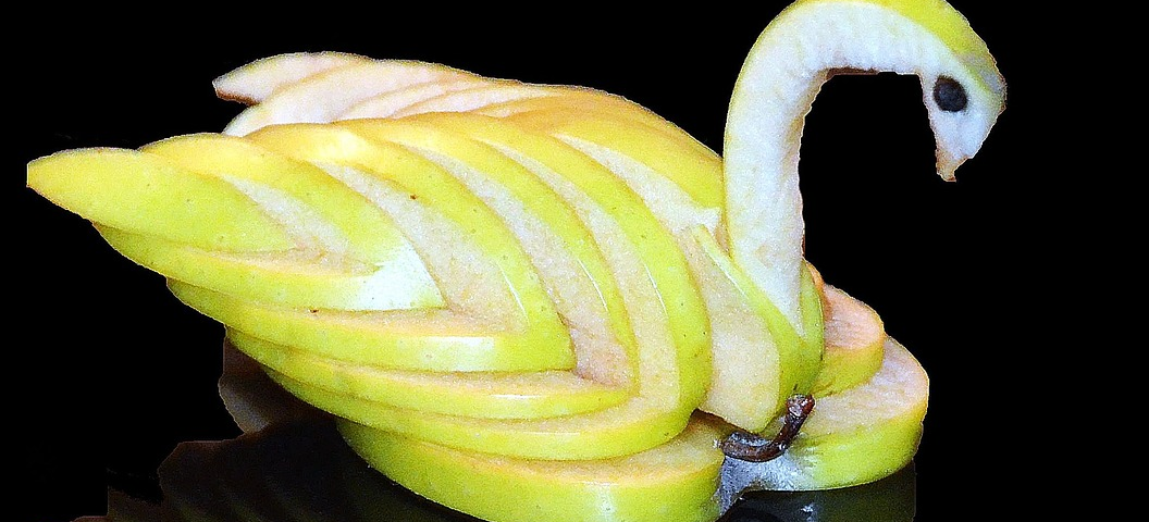 Yellow apple, carved into a swan, sitting on a glossy black surface