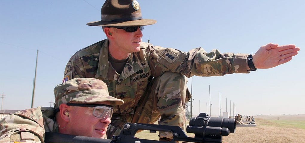 Drill sergeant instructing recruit on rifle range.