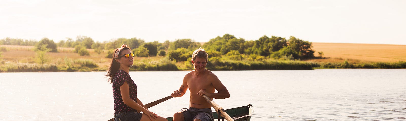 A happy romantic couple rows a boat on a lake. The sun shines softly down on them.