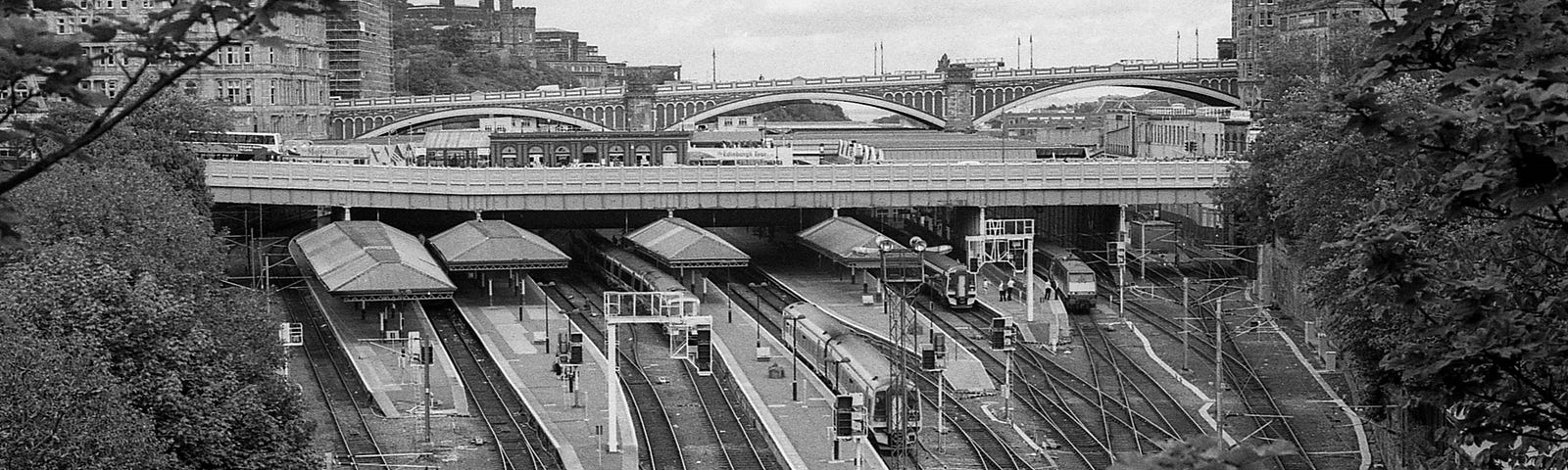 Black and white photo of a train station yard from above, bridges in the background