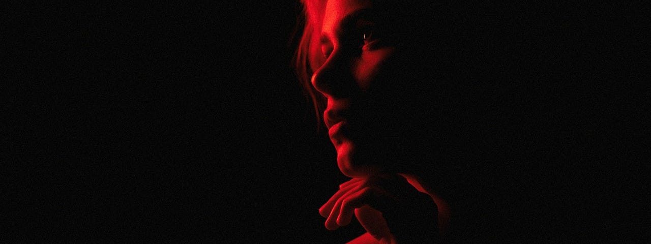 Profile of a woman, looking pensive, her face highlighed by a red light