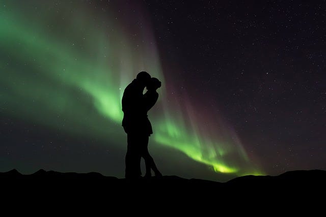 silhouette of a couple (mf) kissing, embracing with background of the northern lights, green yellow lights showing against night sky