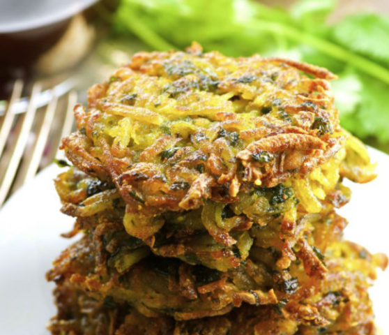 Green and yellow latkes stakced on a white plate outside.