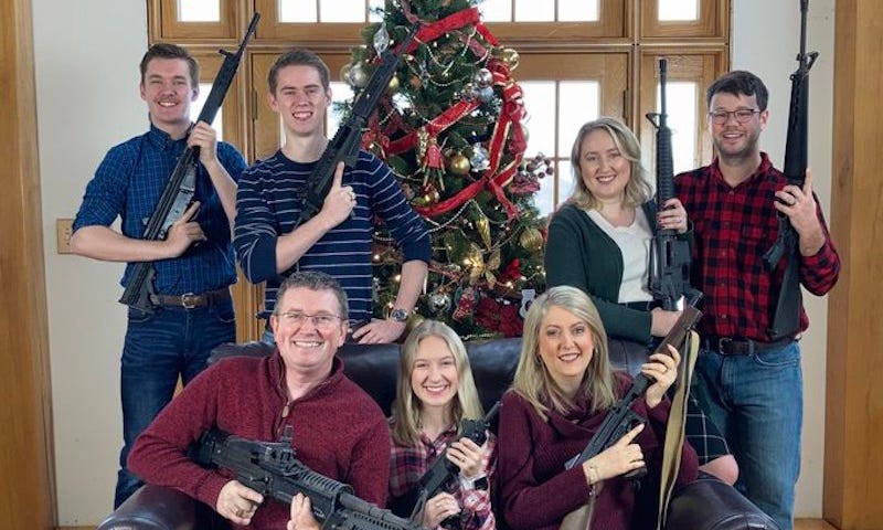 Seven family members holding assault rifles in front of Christmas tree