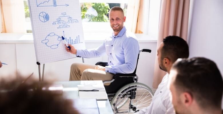 Man sitting on a wheelchair discussing while pointing to an illustration on a white board.