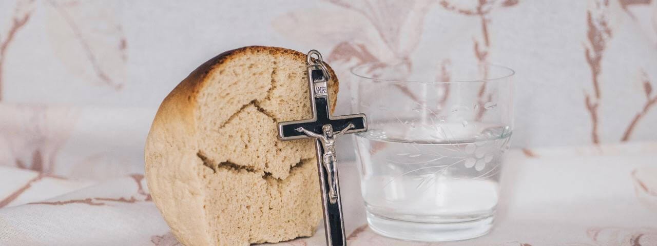 Bread and water, with a small crucifix propped up against the bread