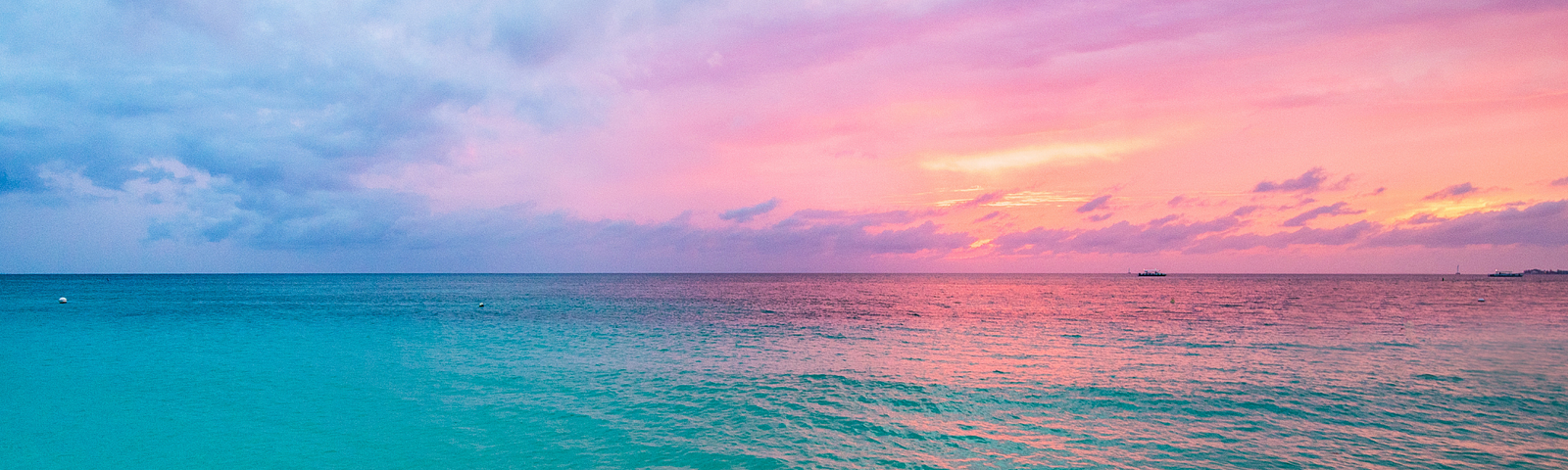 sunrise across a green ocean at the beach with a mix of pink and blue skies and clouds