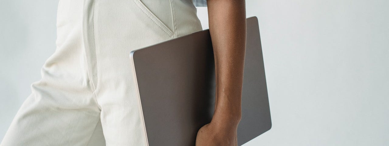 Woman in strikingly simple clothes holding a silver laptop.