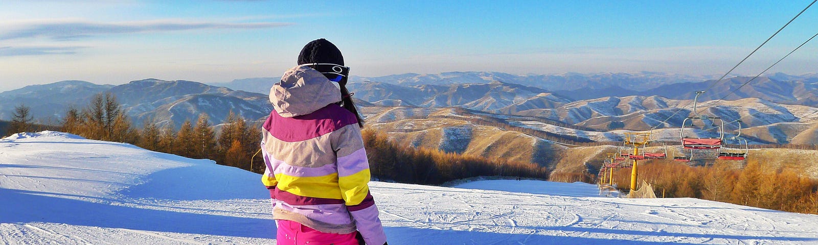 Woman in ski outfit and snowboard looking over ski slope and barren hills