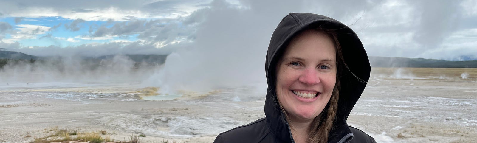 Jackie standing in black zipped hoodie in front of geyser.