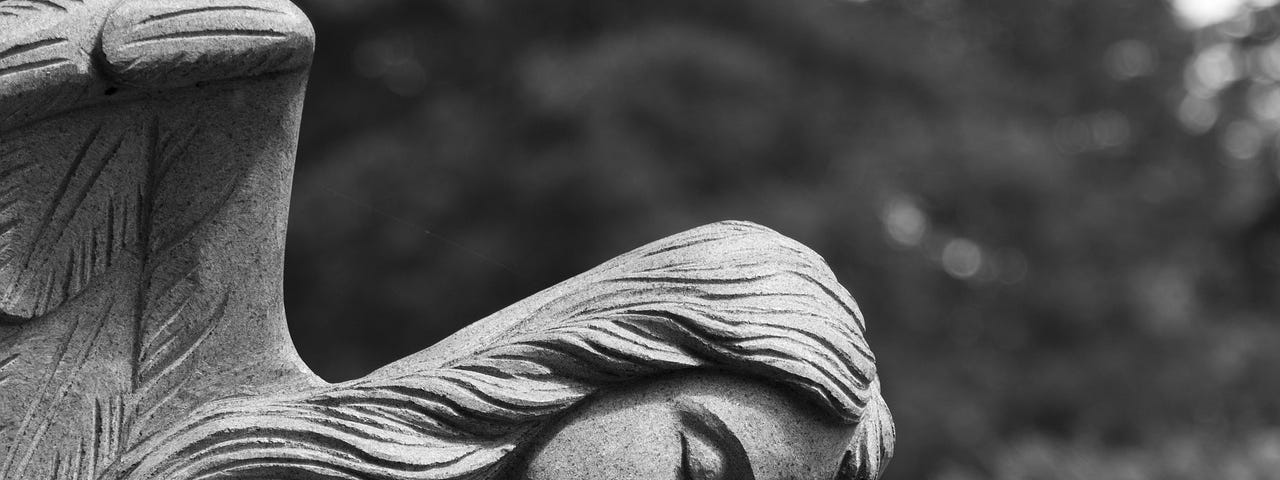 A grayscale image with a concrete angel resting her had on her arm. Everything is gray.