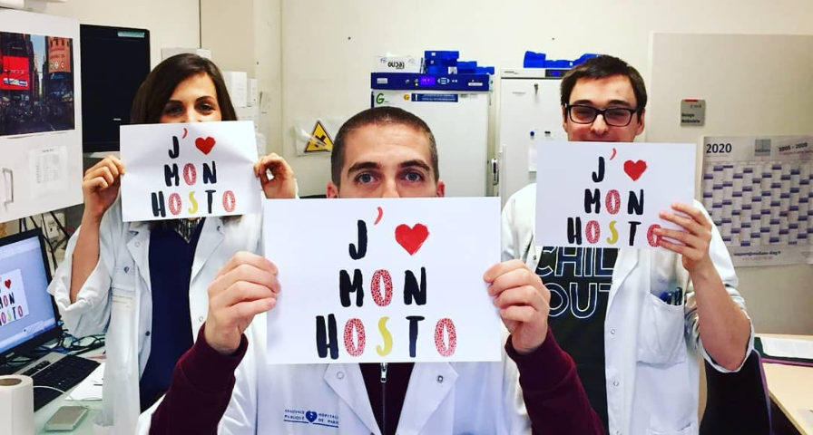 3 doctors in a hospital room, each holding a sign that reads ‘J’aime mon hosto‘