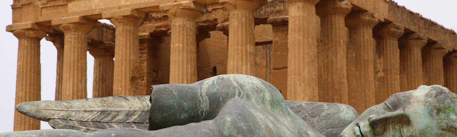 A colour image of a huge sculpture of Icarus by Igor Mitoraj lying in front of one of the Greek temples outside Agrigento