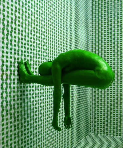 artistic photo of green-skinned person appearing to stand on a wall with a white and green patterned wallpaper