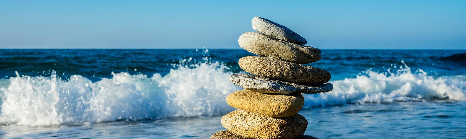 Rock cairn with 8 rocks stacked on sandy beach, with ocean waves in the background. Wave breaking with white surf.