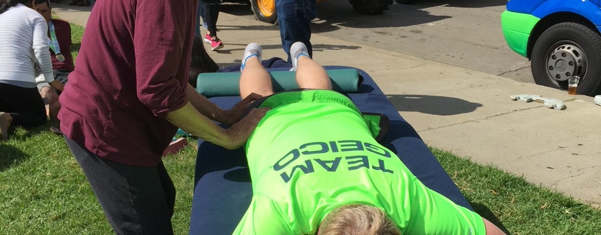A runner gets a post-race massage on a lawn next to a sidewalk