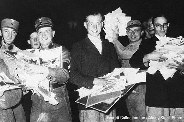 Nazi Storm Troopers and young German men holding pictures and pamphlets at a public book burning, circa 1933–1940.