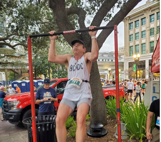 A man outdoors is outdoors doing a pullup on a pullup bar.