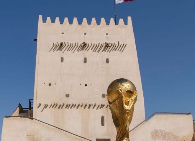 A picture of the World cup trophy and football in front of a lighthouse flying the Qatar flag. This is a promotional photo for the 2022 Qatar World Cup.
