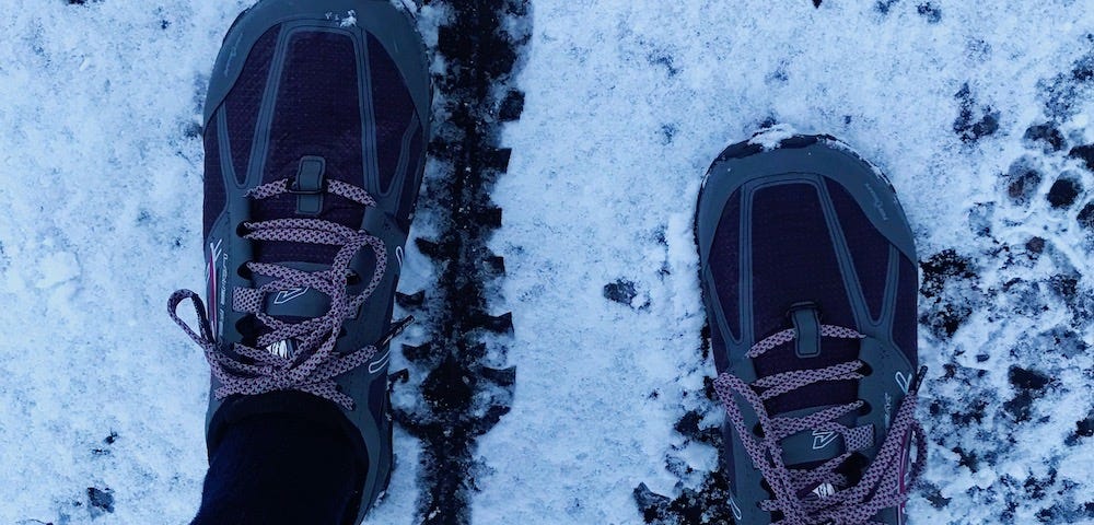 Feet in trail shoes standing on a snowy road