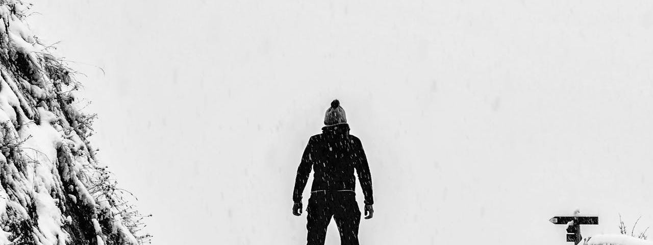 A person wearing all black clothing stands atop a snowy hill.