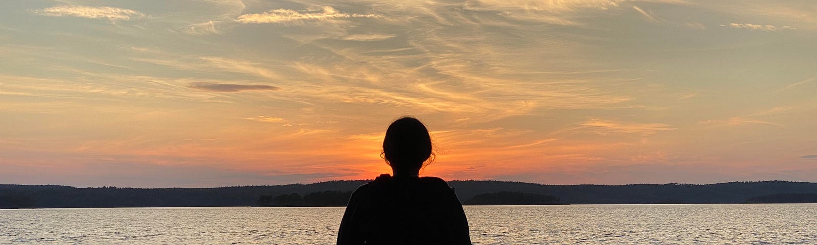 The author is sitting by a lake, facing the sunset in Sweden
