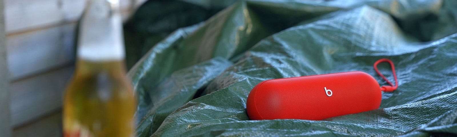 A red Beats Pill outside on a green tarp. A beer in the foreground.