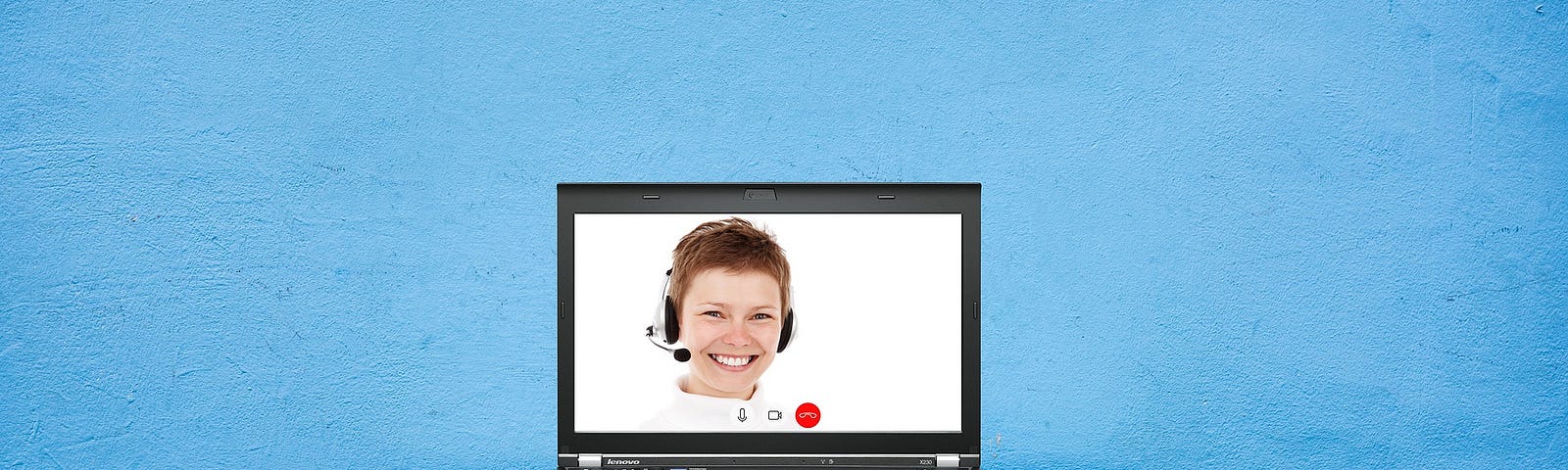 A laptop opened to a person smiling and wearing a headset