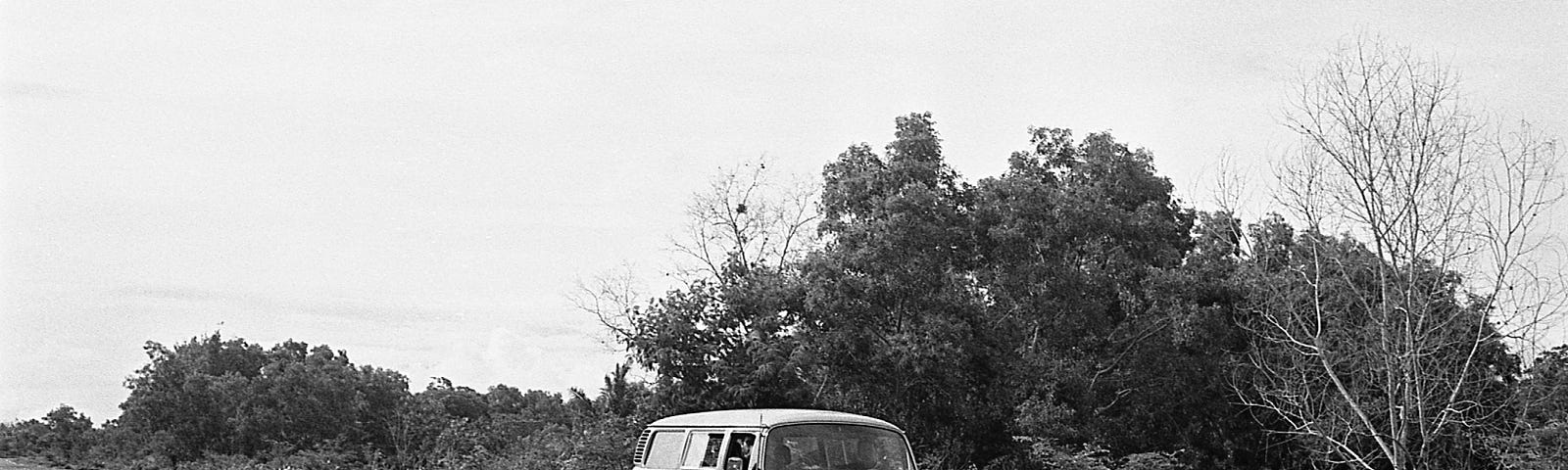 Black and white photo of V.W. van driving along a highway with trees in the background.