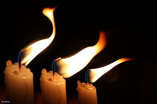 Three candles with flames being blown by a breeze