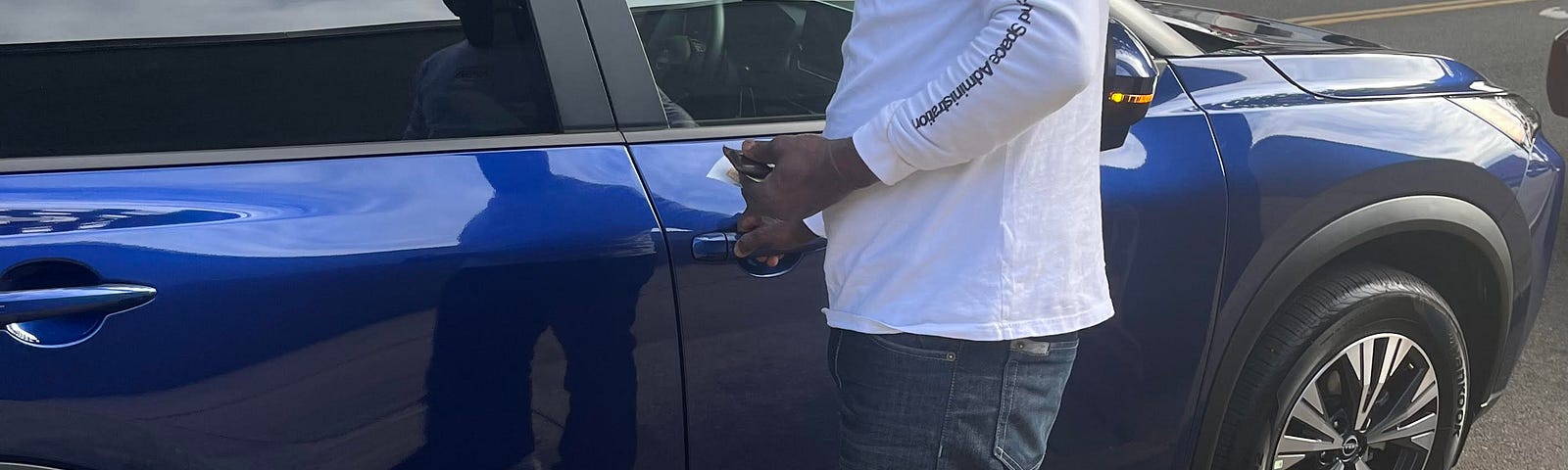 Dark skinned man putting key into car lock on passenger side of navy blue SUV cross vehicle.