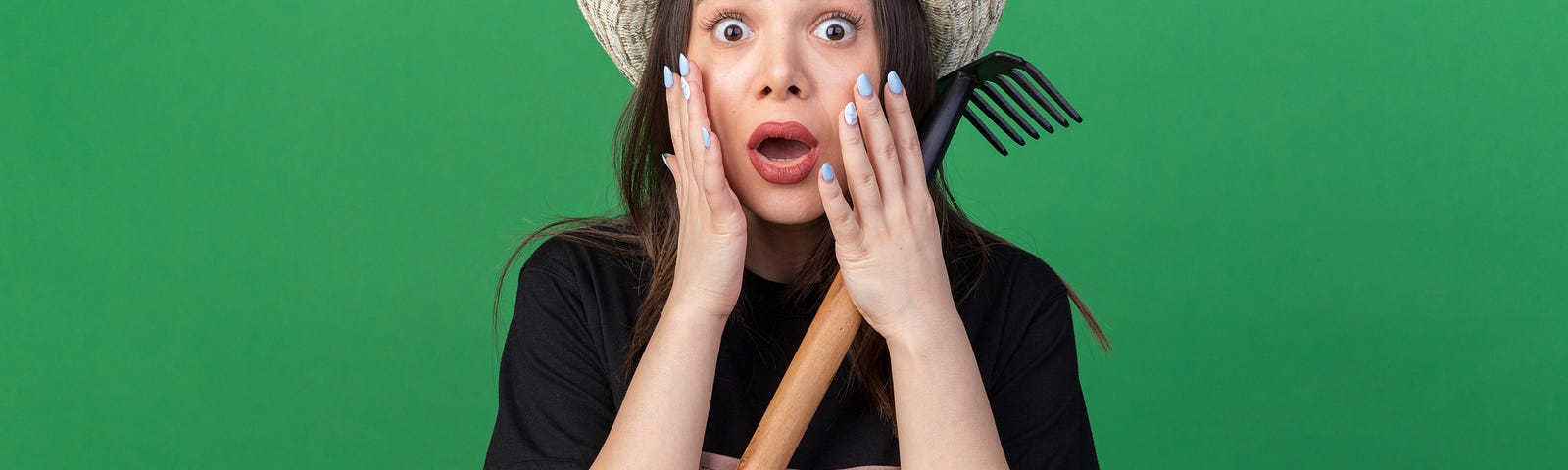 female gardener holding small rake and looking shocked against green background